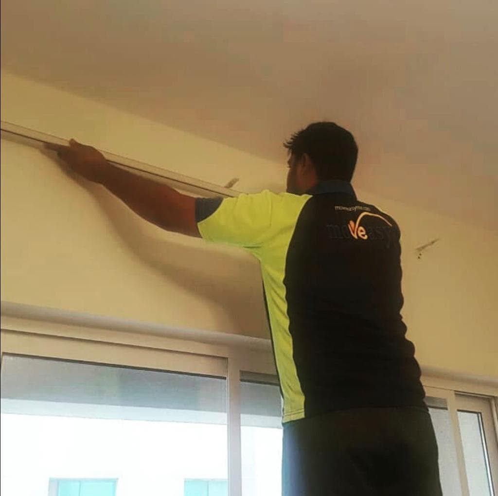 A moveeasy staff member in branded uniform installing curtains in a newly moved-into home